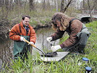 Rita Jack, Michigan Water Sentinels Director, works with volunteer Murray Borello to take samples of stream sediment.